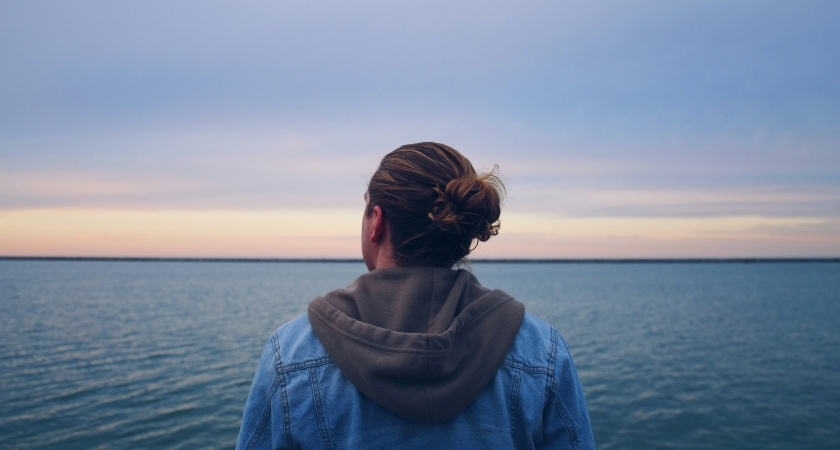 hombre con chaqueta de mezclilla azul de pie cerca del cuerpo de agua durante el dia